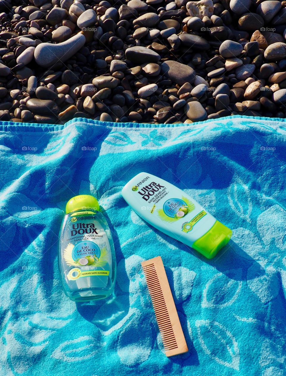 Garnier eau de coco shampoo and conditioner on blue beach towel with beach stones and a wood comb.