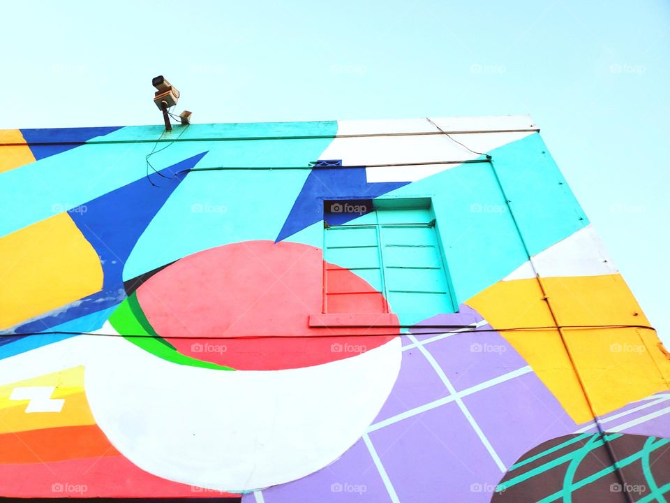 Retro, fun, bright, colorful street art on building wall with old style window and CCTV camera.