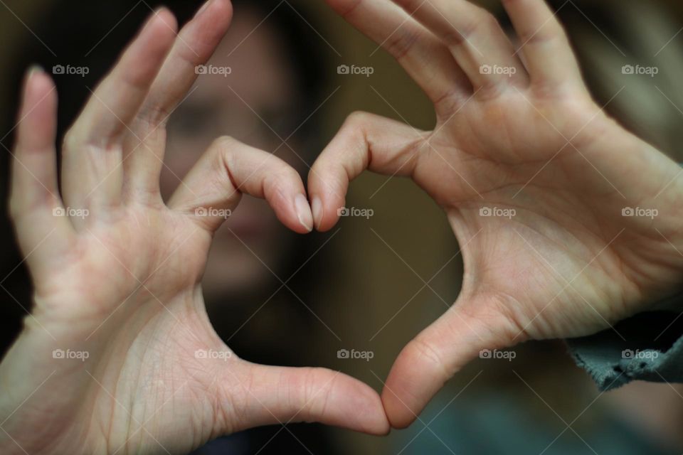 A couple's hands and fingers are shaped into a heart as a sign of love