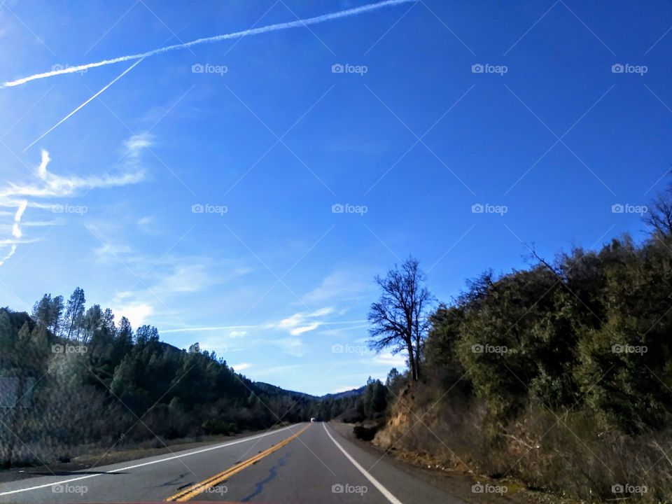 two lane road nestled between hills. chemtrail in clear blue sky