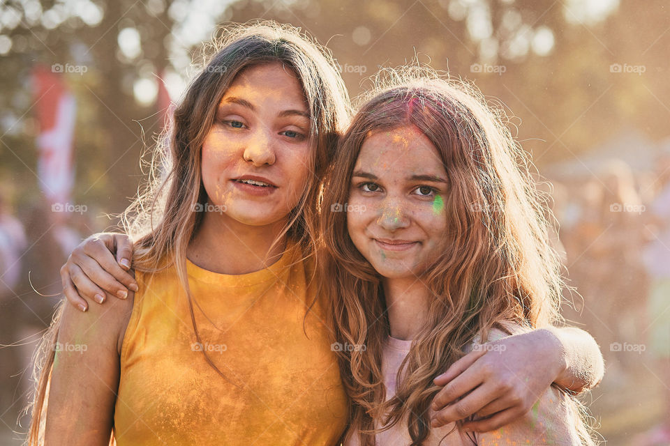 Portrait of happy smiling young girls with colorful paints on faces and clothes. Two friends spending time on holi color festival. Real people, authentic situations