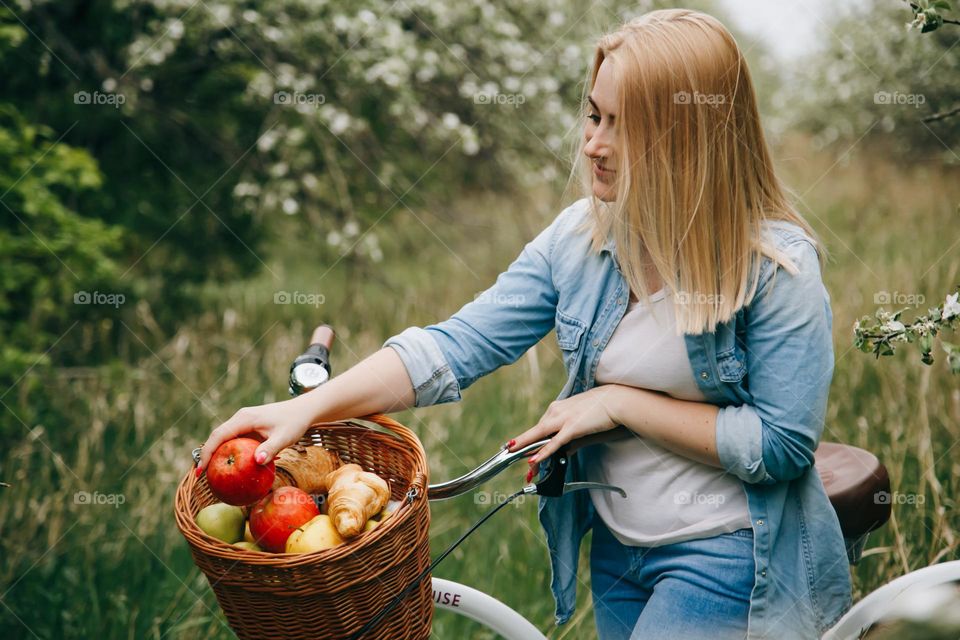 Blonde girl in jeans clothes put apple in basket on bicycle