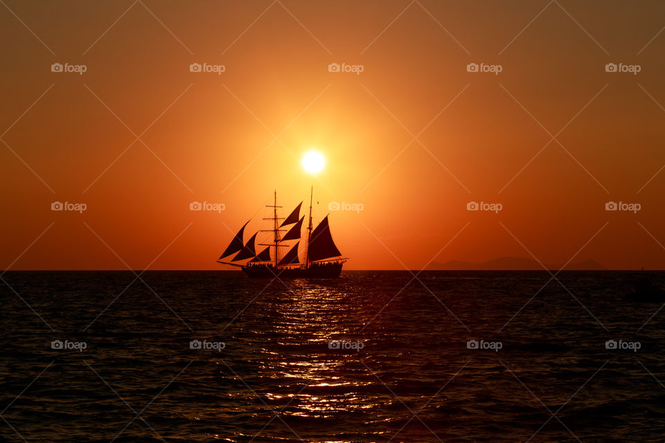 Sunset and a sailing ship in Santorini, Greece.. The sun is going down while a sailing ship is passing by
