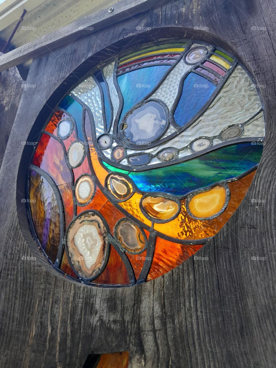 stained glass bubbling and circling in a tall. wooden wall, with pure sunlight shining through.