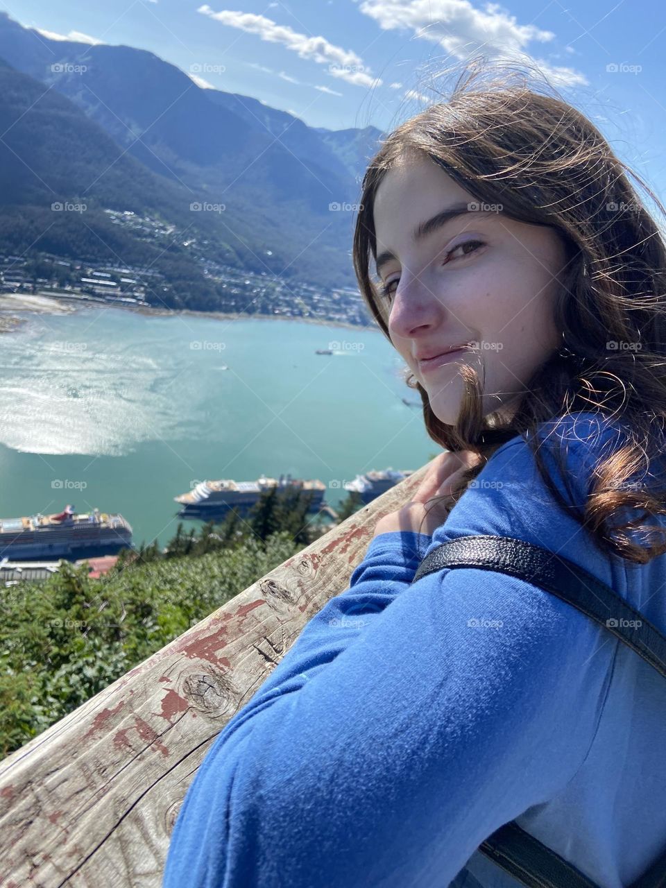 Girl wearing a blue shirt looking down from a mountain of a view of cruise ships in Alaska.