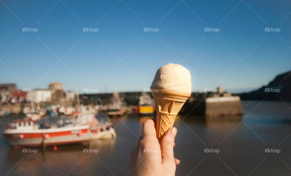 An outstretched hand holds out an ice cream in front of the harbour at Mevagissey, Cornwall UK 