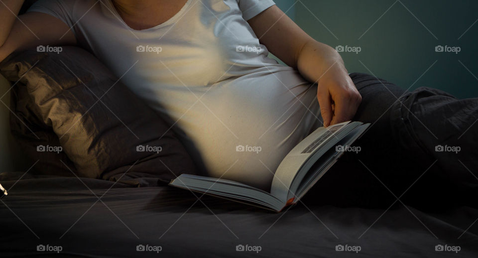 Pregnant woman relaxing in bed all day with a book to read. 