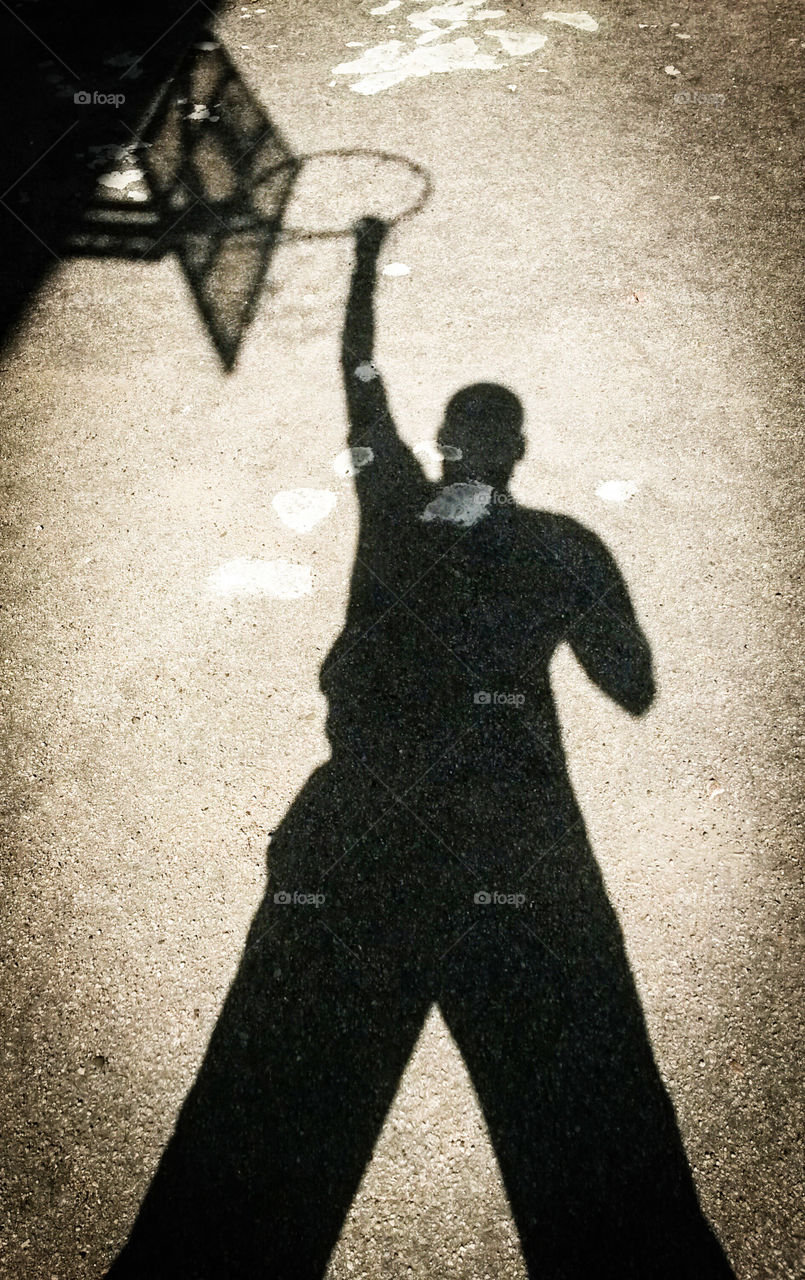 Shadow of a man hanging on basketball hoop