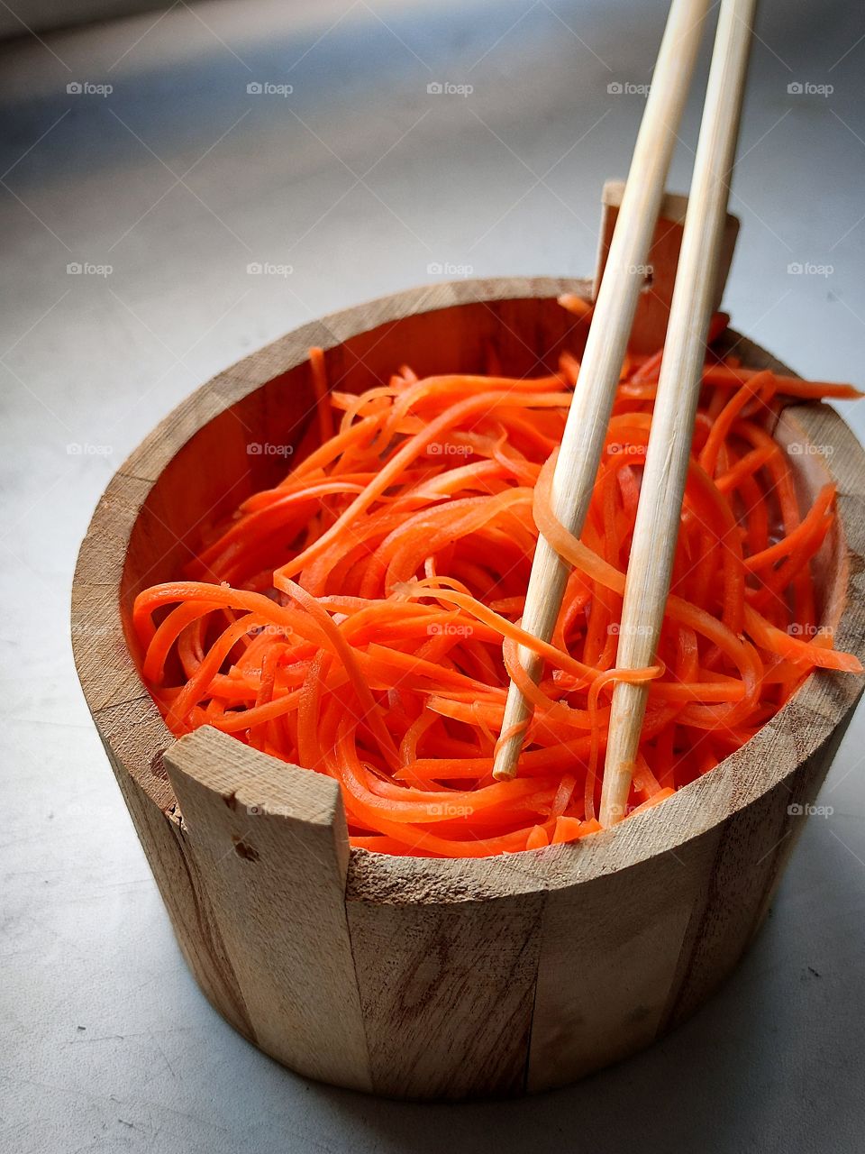 A wooden tub containing chopped carrots with spices.  Two wooden chopsticks are inserted into the carrots
