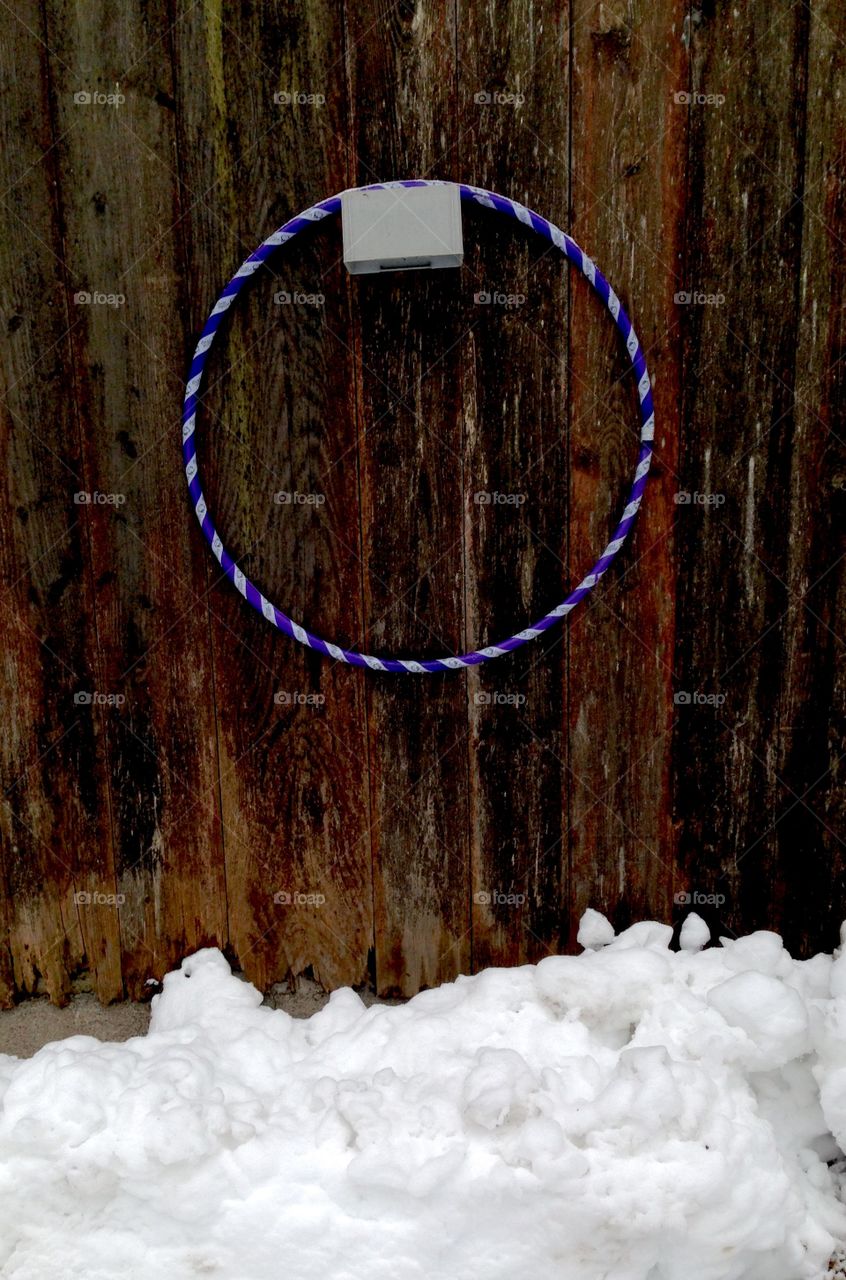 Hula hoop ring hanging on a wooden wall in the winter with some snow on the ground 