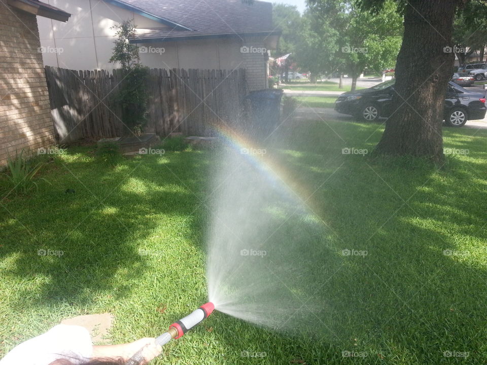 Rainbow by hose. Daughter spraying water making rainbow.