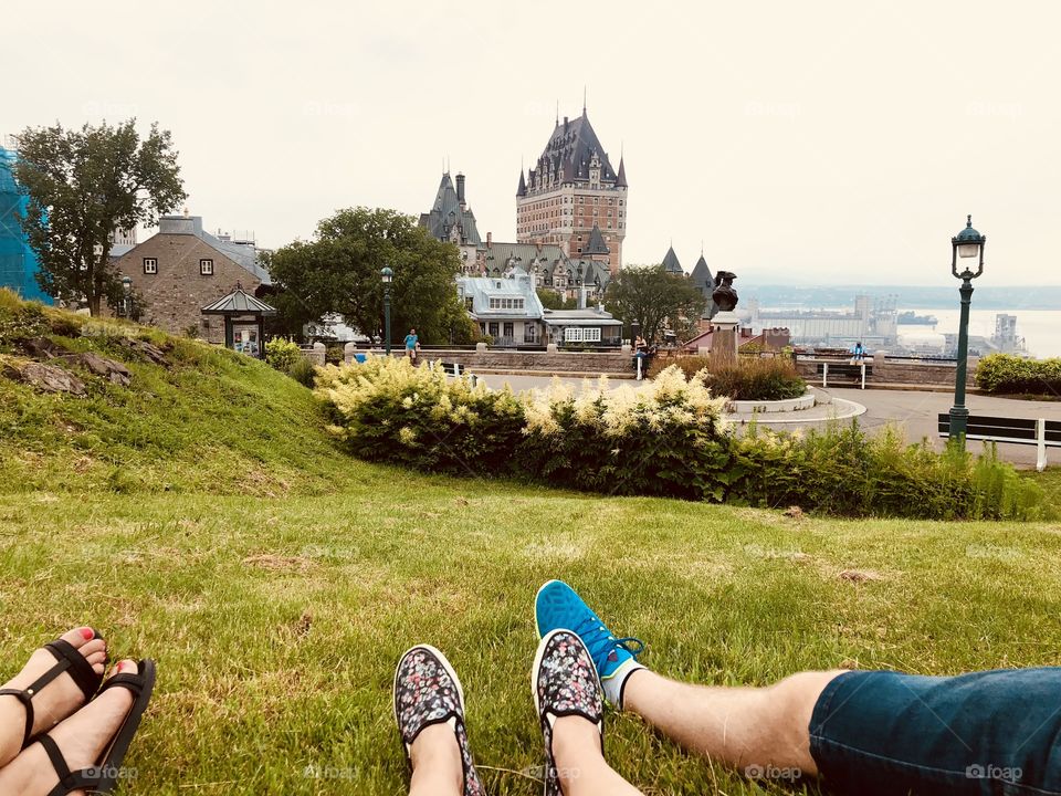 People showing legs while laying on the green grass to view the Chateau Frontenac castle and St Laurent river in Quebec city