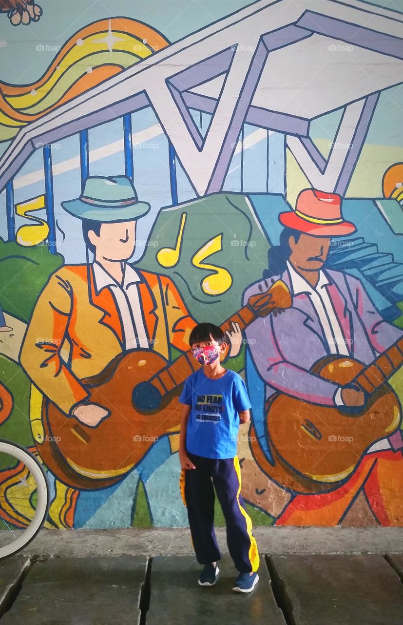 A boy with mask standing in front of mural wall.