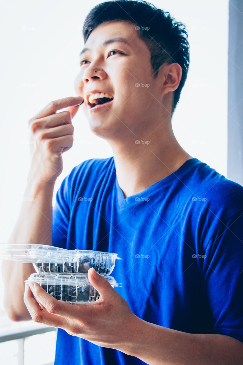 Young man holding and eating fresh blueberries in plastic boxes 