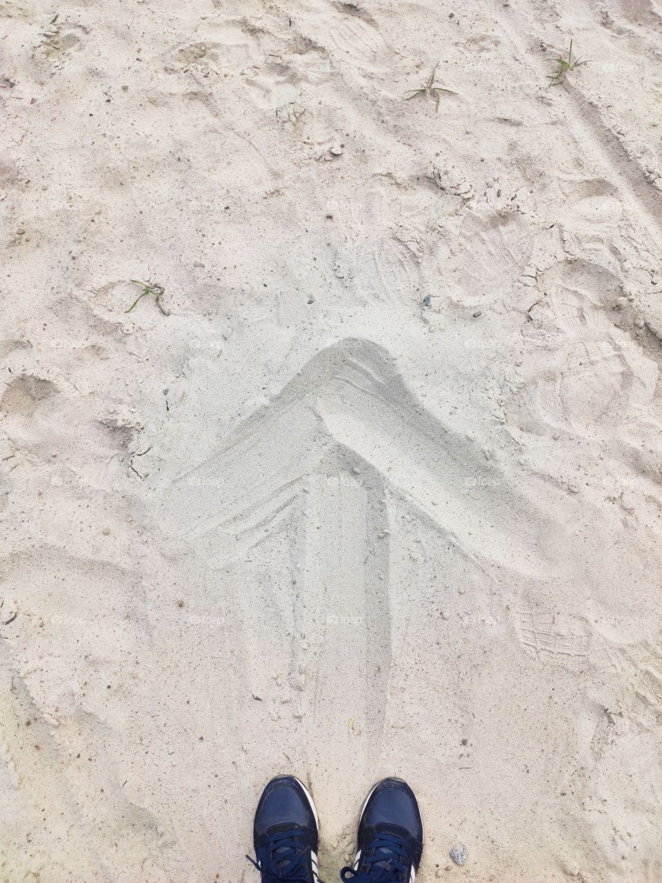 On the beach are a pair of sneakers and a drawn arrow on the sand