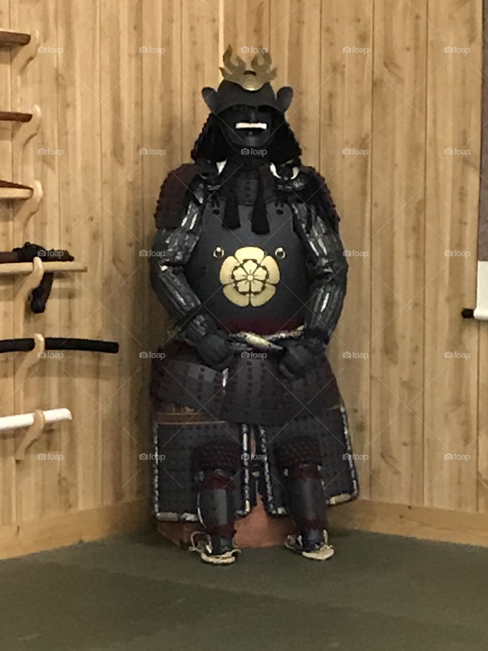 Black samurai armor sitting in the corner all by its lonesome, waiting to be worn by someone who wants to be a samurai at the dojo for the day.