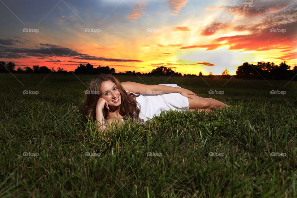 Smiling young woman lying on grass with dramatic sky