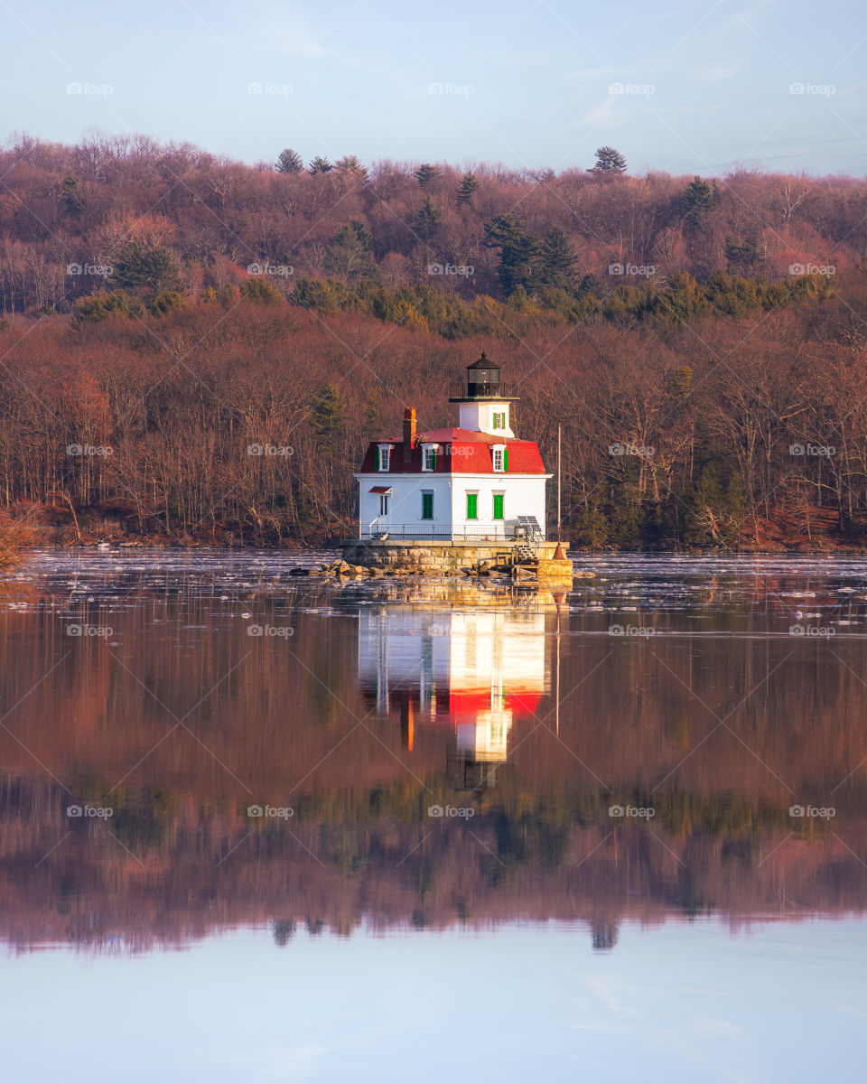 Lone white and red lighthouse reflecting in a lake, popping out from the wooded background