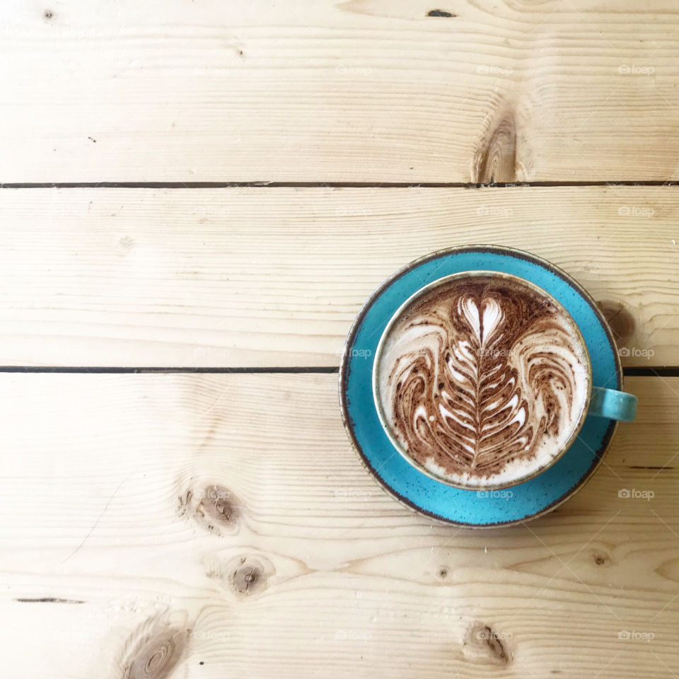 A photo taken of a Mocha coffee. The photo was taken in a local cafe in Wales, and features a lovely vintage retro blue mug, placed on a knitted wooden panel table. The mocha also features a coffee pattern