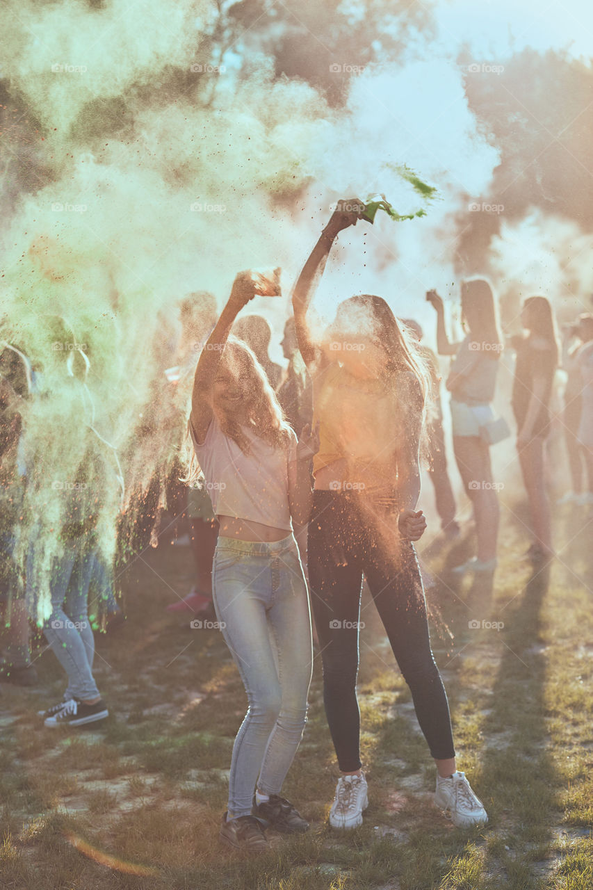 Portrait of happy smiling young girls with colorful paints on faces and clothes. Two friends spending time on holi color festival. Real people, authentic situations