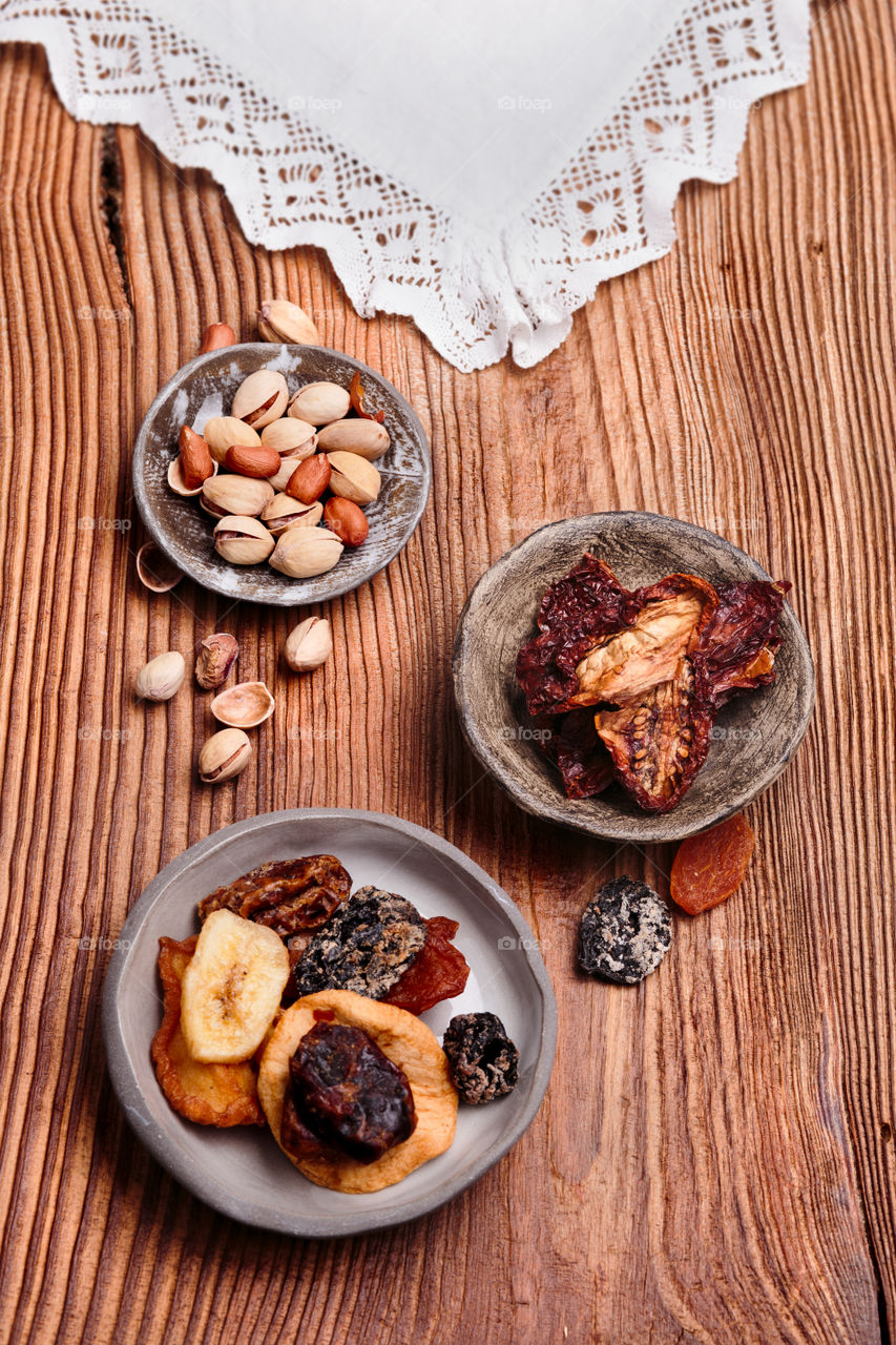 Dried fruits and nuts in handmade pottery bowls on old wooden table from above