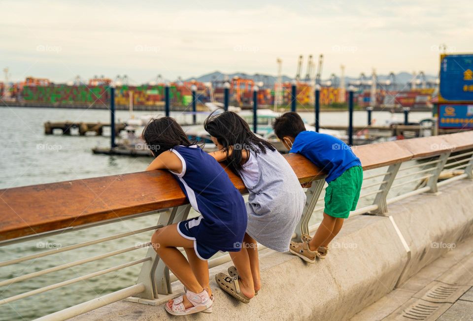 Kids climbing the fence of an ocean.