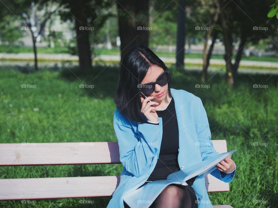 Business woman using her smartphone while sitting on the park bench 