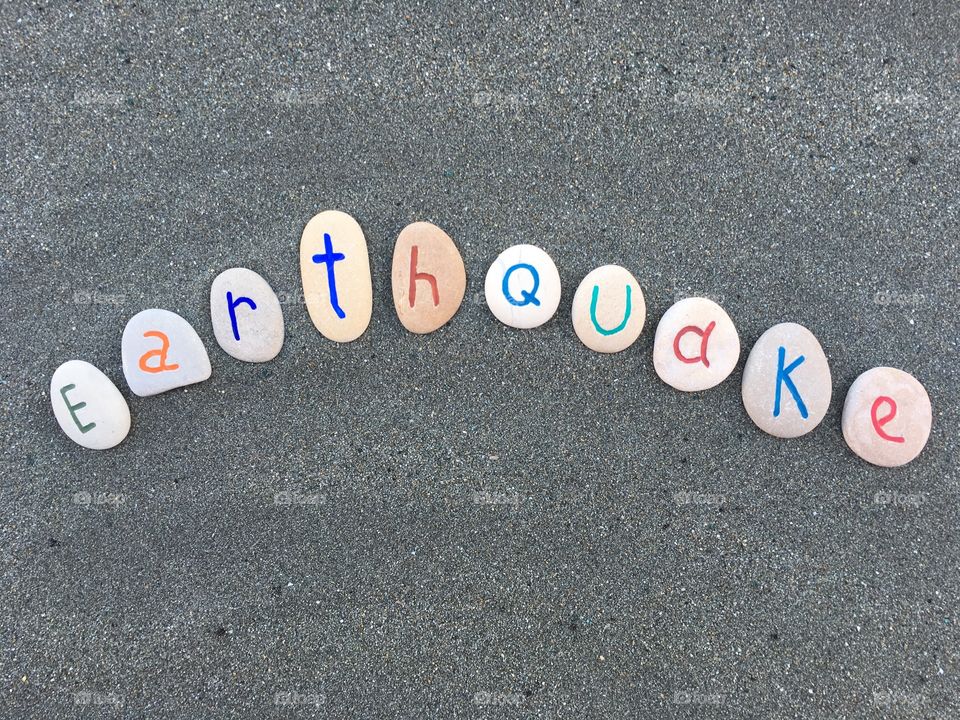 Earthquake word with stone letters over black sand 