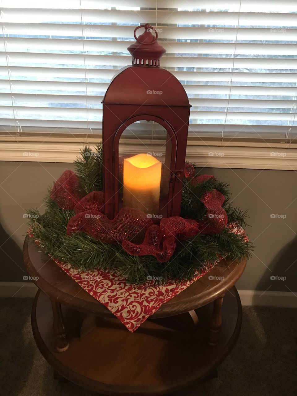 A red lantern holding a glowing candle set among some greenery and red ribbon creates a beautiful Christmas touch.