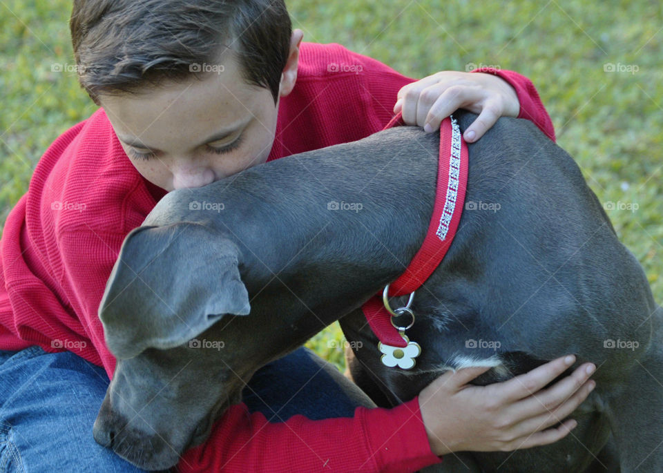 A boy on the grass hugging his dog