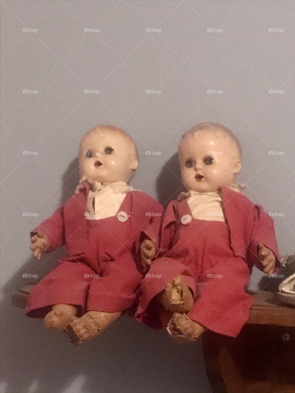 Antique twin dolls wearing matching red velvet suits sitting on a shelf in front of a blue wall