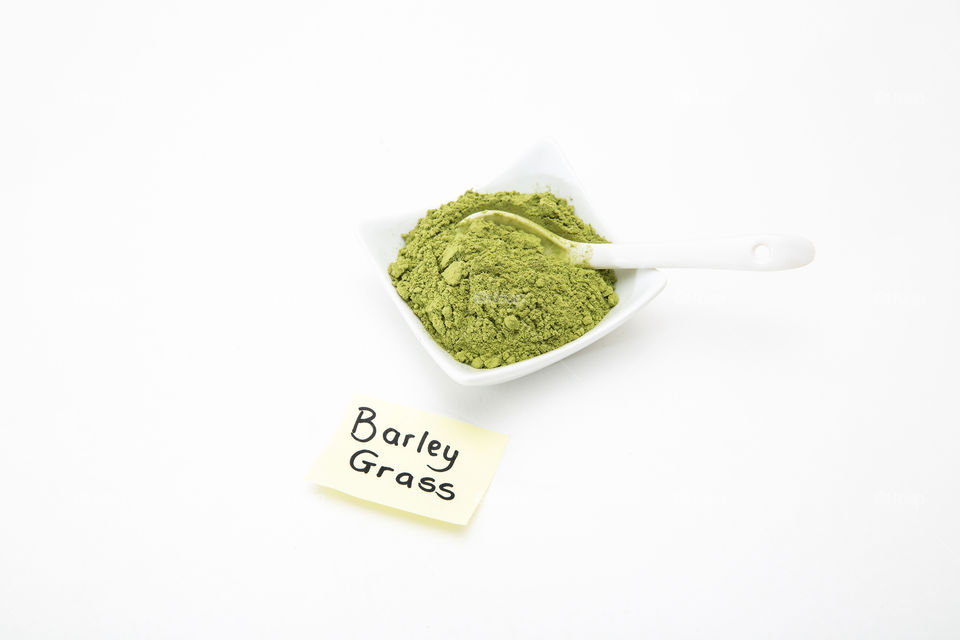 Health product - barley grass green powder in white bowl with white spoon on white background. Barley grass note.