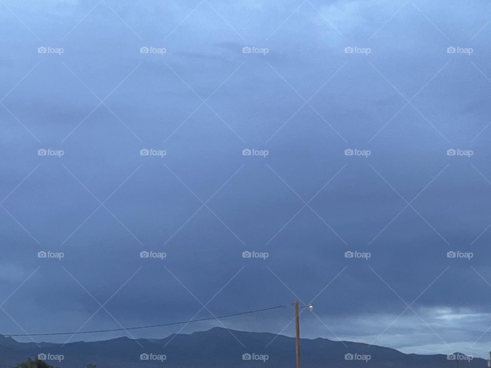 A dark grey and blue sky with clouds and mountains.