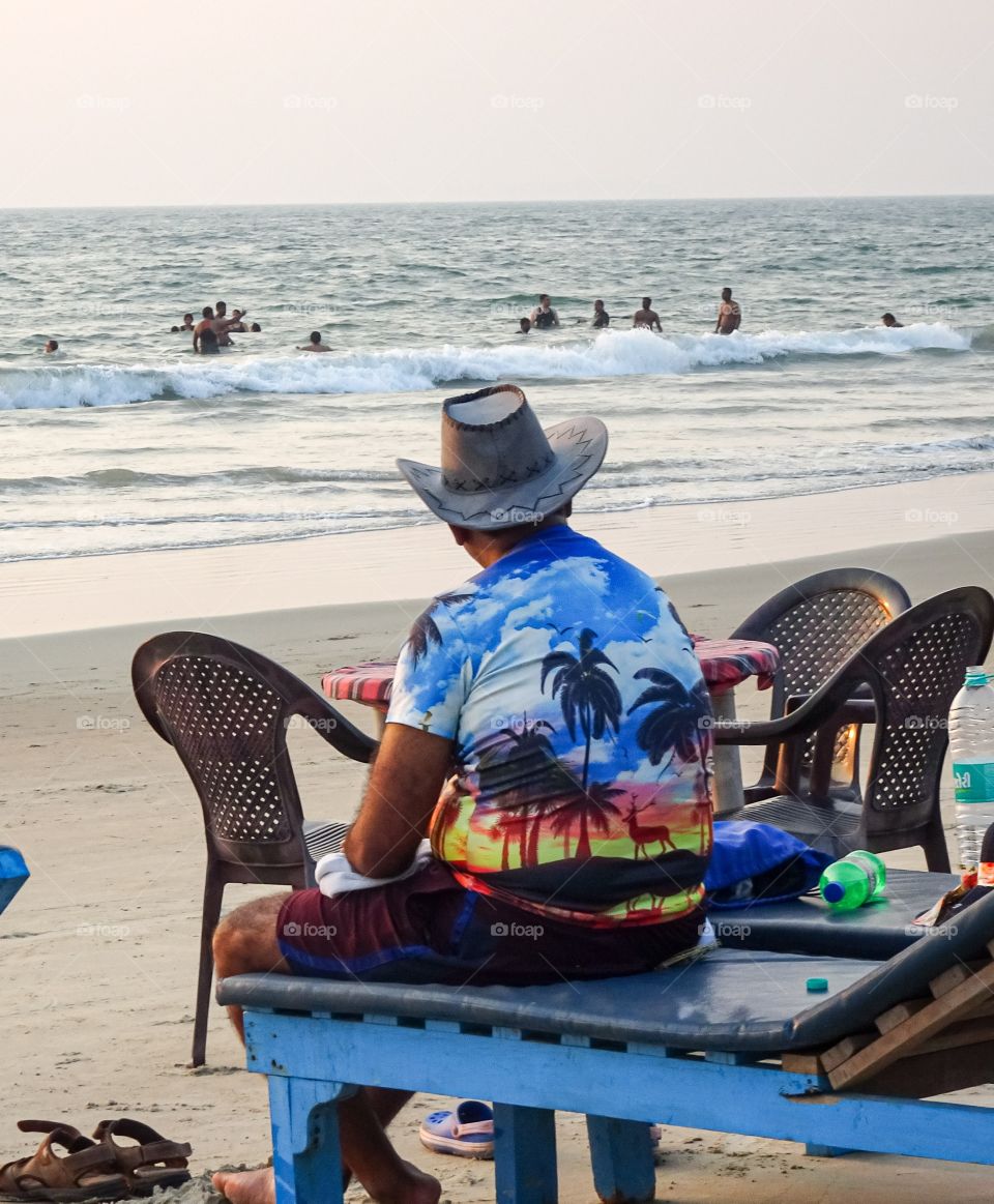 man wearing cowboy hat and a colorful Hawaiian shirt sitting at beach in summer