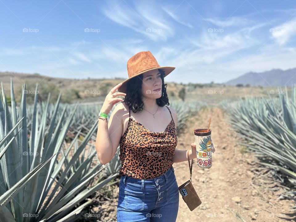 Woman wearing a hat while holding a glass in her hand looking at the horizon.