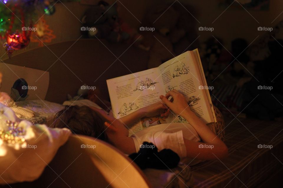 Girl reading a book in bed under the Christmas tree