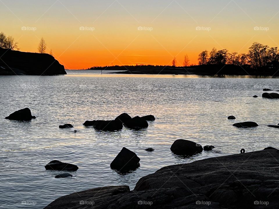 Beautiful tranquil orange sunset landscape over the mirror smooth sea water surface with dark stones on the foreground 