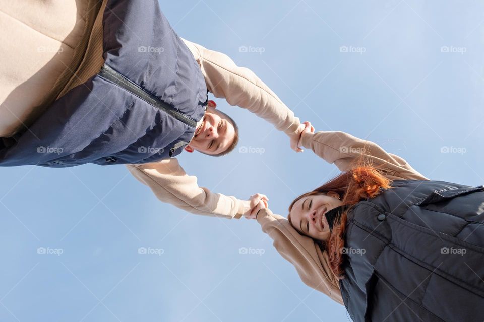 couple holding hands on sky background, view from below