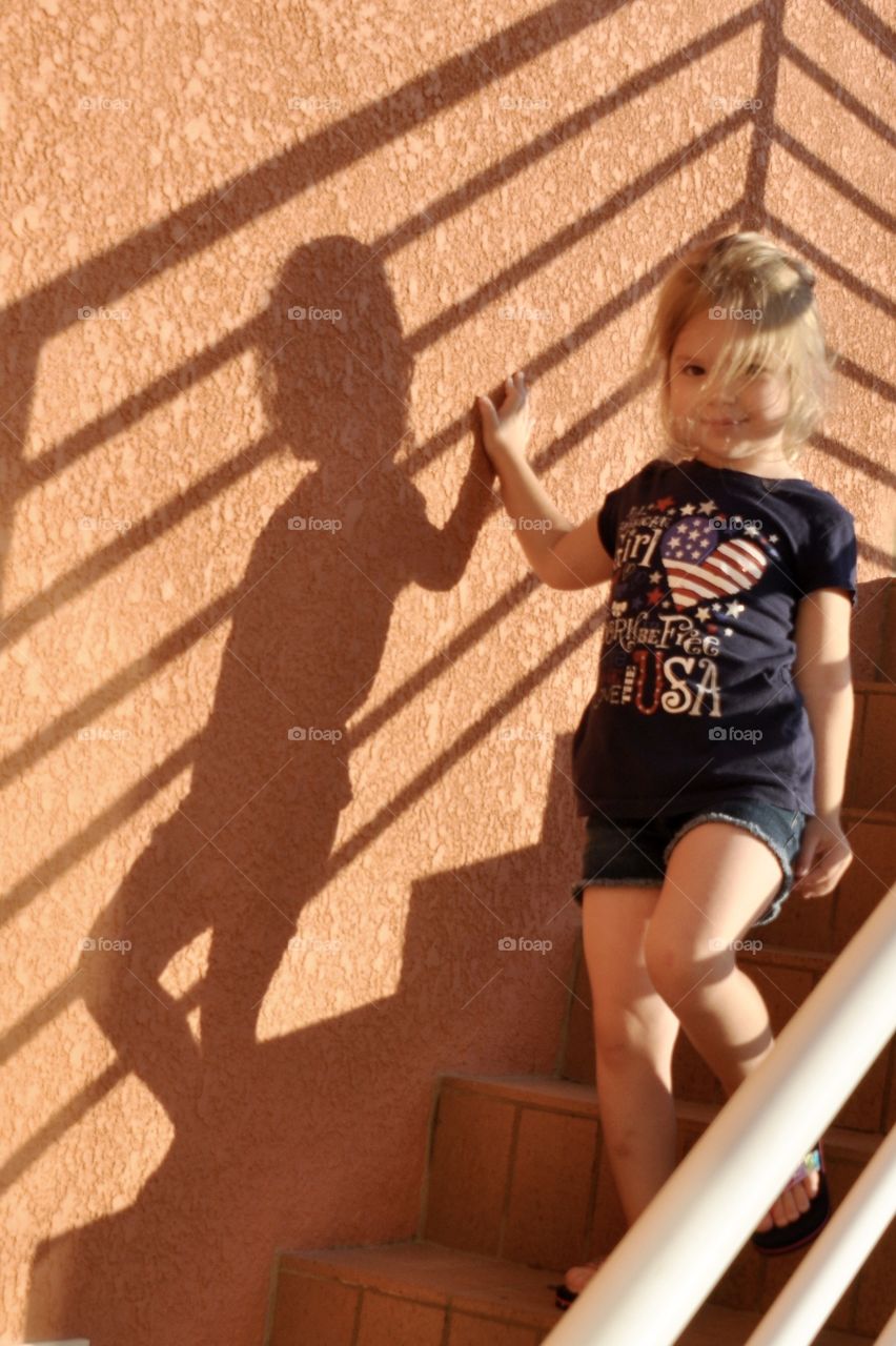 Little girl walking down the stairs with a strong shadow cast on the wall 