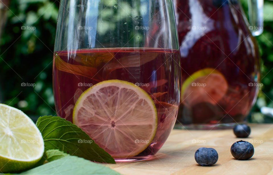 Beautiful fresh summer fruit flavored water with citrus, mint herb and antioxidant rich blueberry in glass next to pitcher on wood table low angle view gourmet food and drink photography background