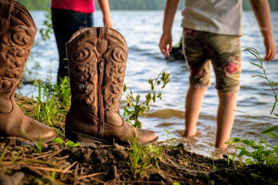 Little girls kick off their cowgirl boots to wade in the lake and feel the mud squish through their toes. Lake Benson Park, Garner, North Carolina. 