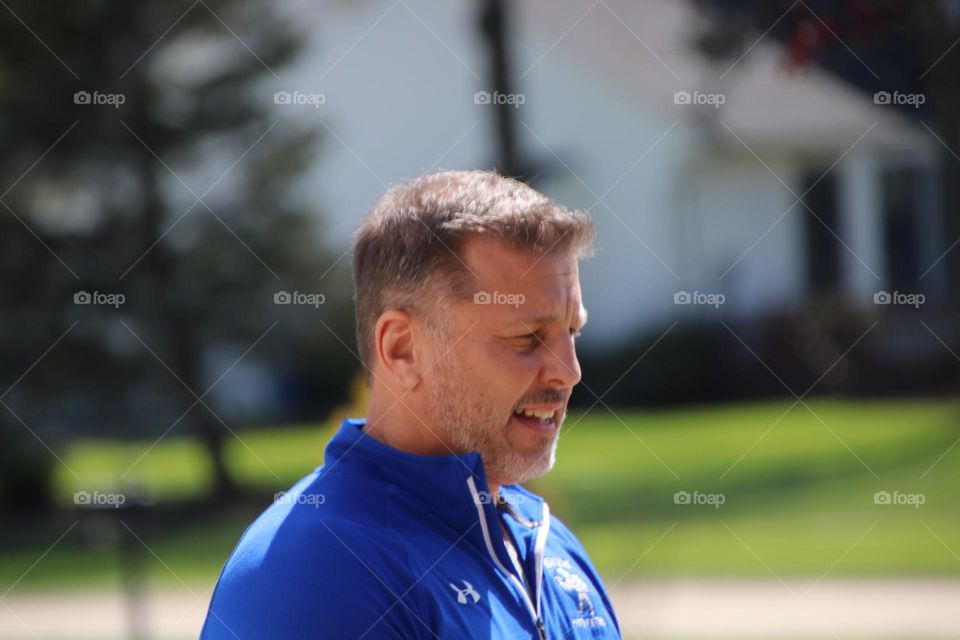 Man with short beard smiling wearing blue shirt outdoors on sunny day 