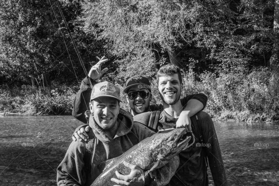Three friends holding fish in hand at lake side