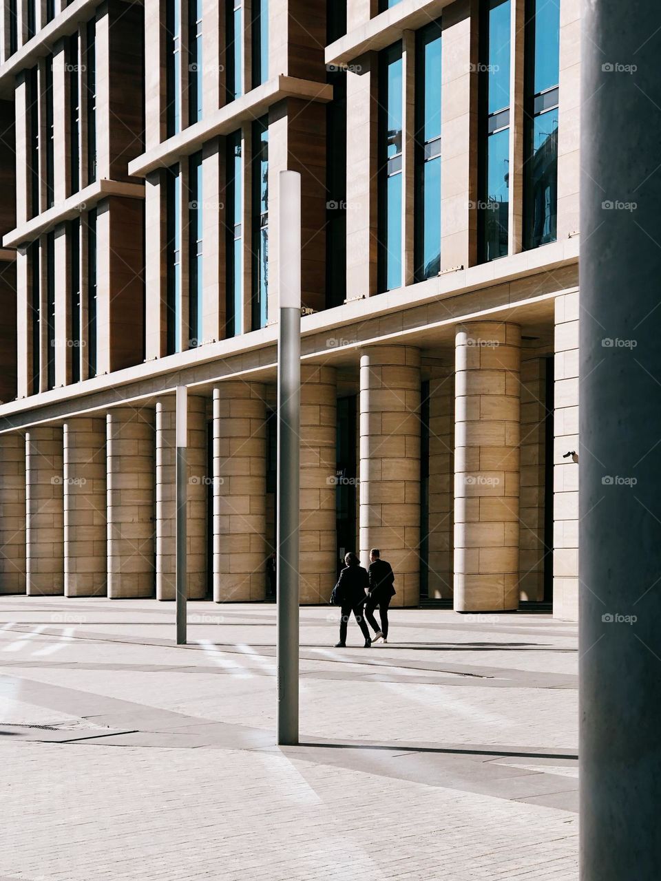 Two people walking near modern building in sunny spring day