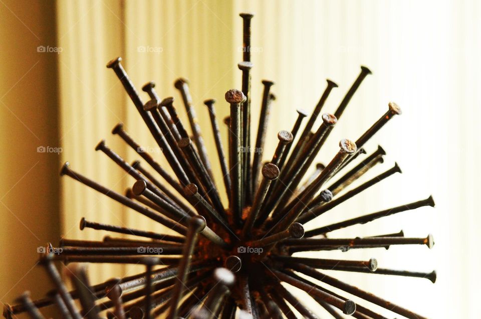 An art piece of metal rustic nails in the shape of a spherical sculpture rest on top of a bedroom dresser.