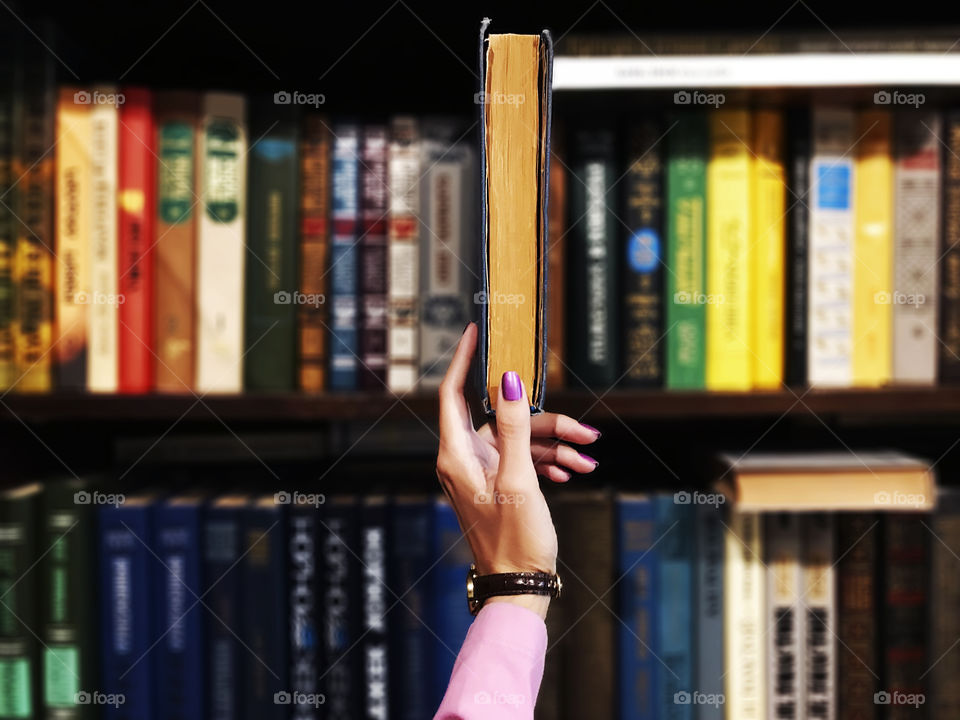 Female hand taking an old book from the bookshelf in the library or bookstore to read 