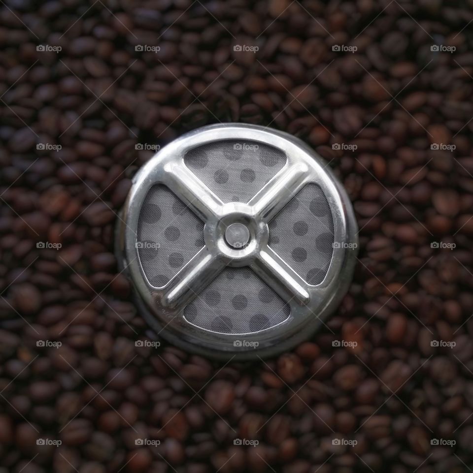 French press coffee maker strainer on a bed of whole coffee beans