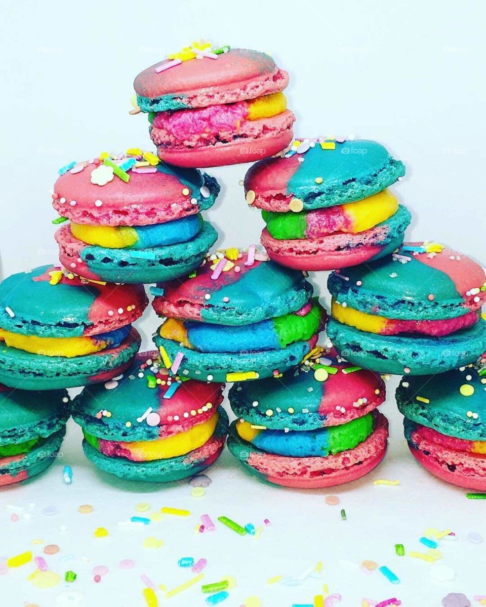 Rainbow sprinkle French macaron stacked in a pyramid. Sandwiched pink and blue shells filled with rainbow coloured filling.