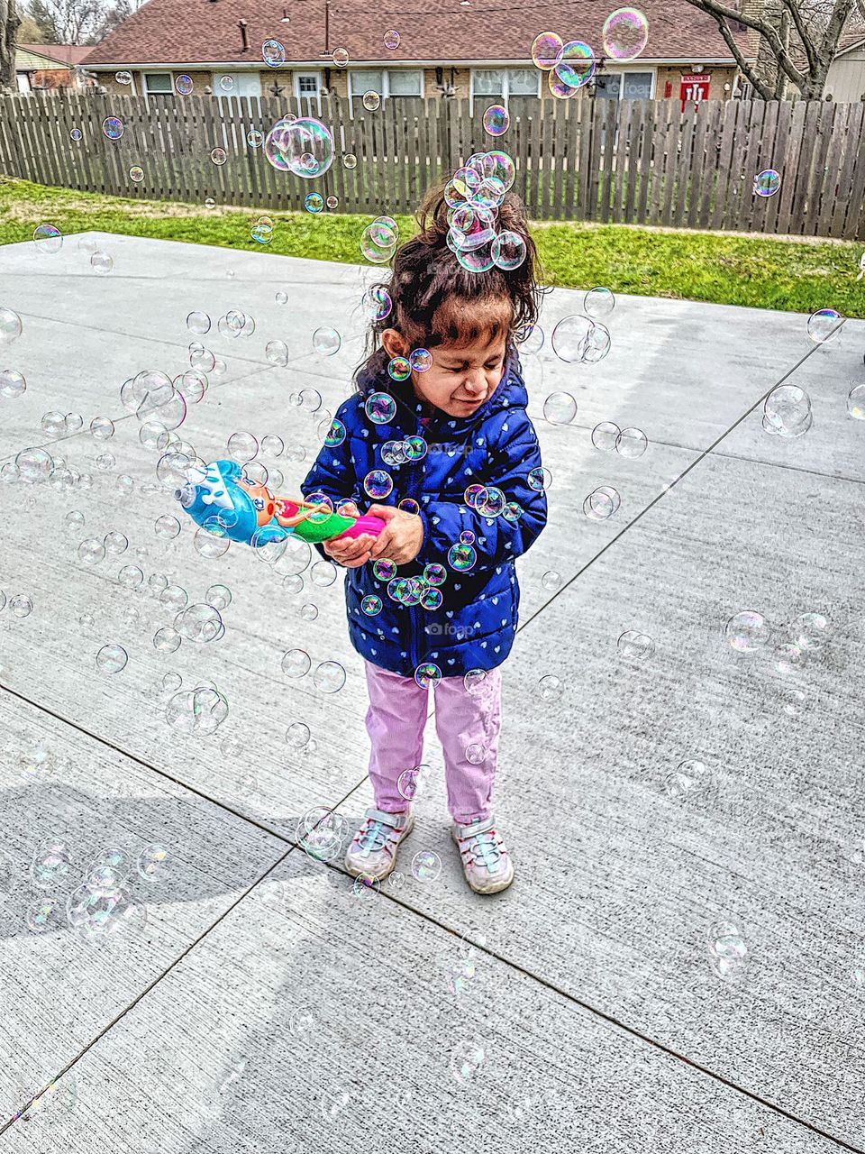 Toddler blowing bubbles outside gets bubbles in her face, surprised by bubbles in the face, toddler plays with bubble maker, circular objects in everyday life, geometric shapes in life, playing with toddlers outdoors, having fun with bubbles 