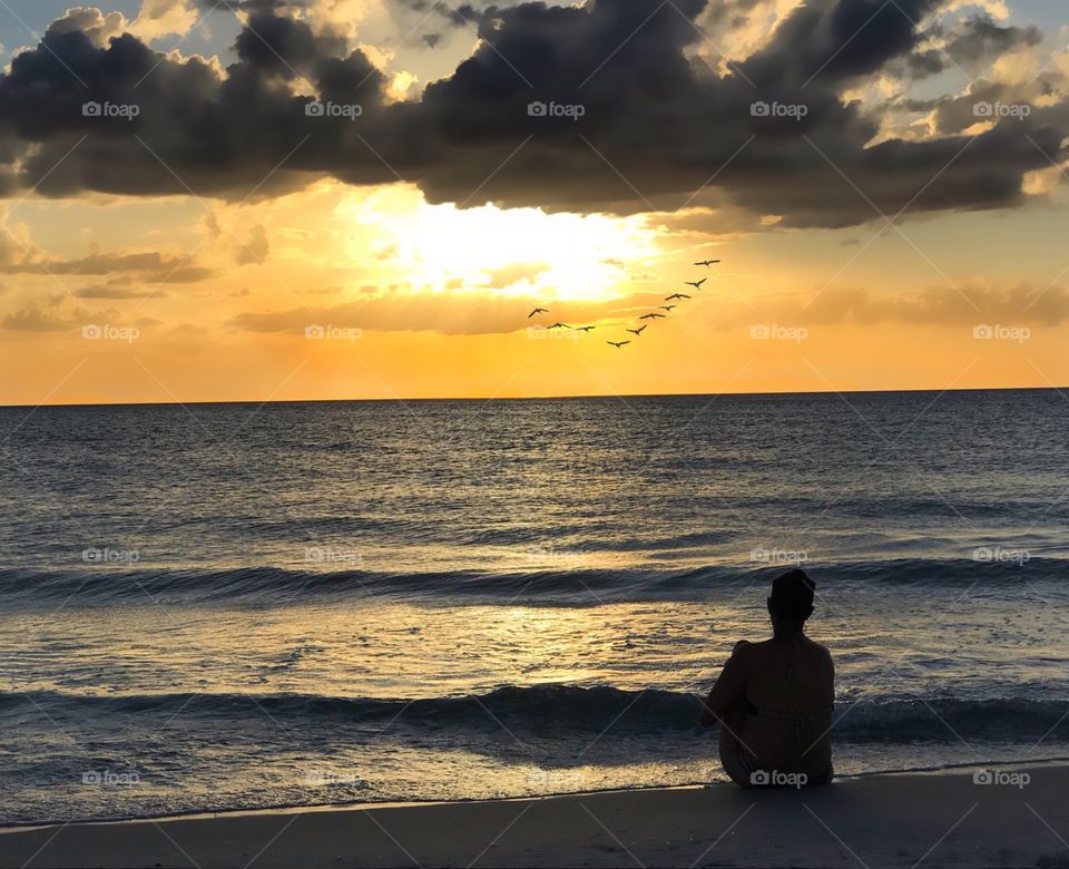 Beachcomber relaxes to watch a gorgeous sunset and a flock of seabirds going home to roost.